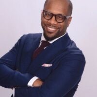 A man in a suit and glasses smiling for the camera.