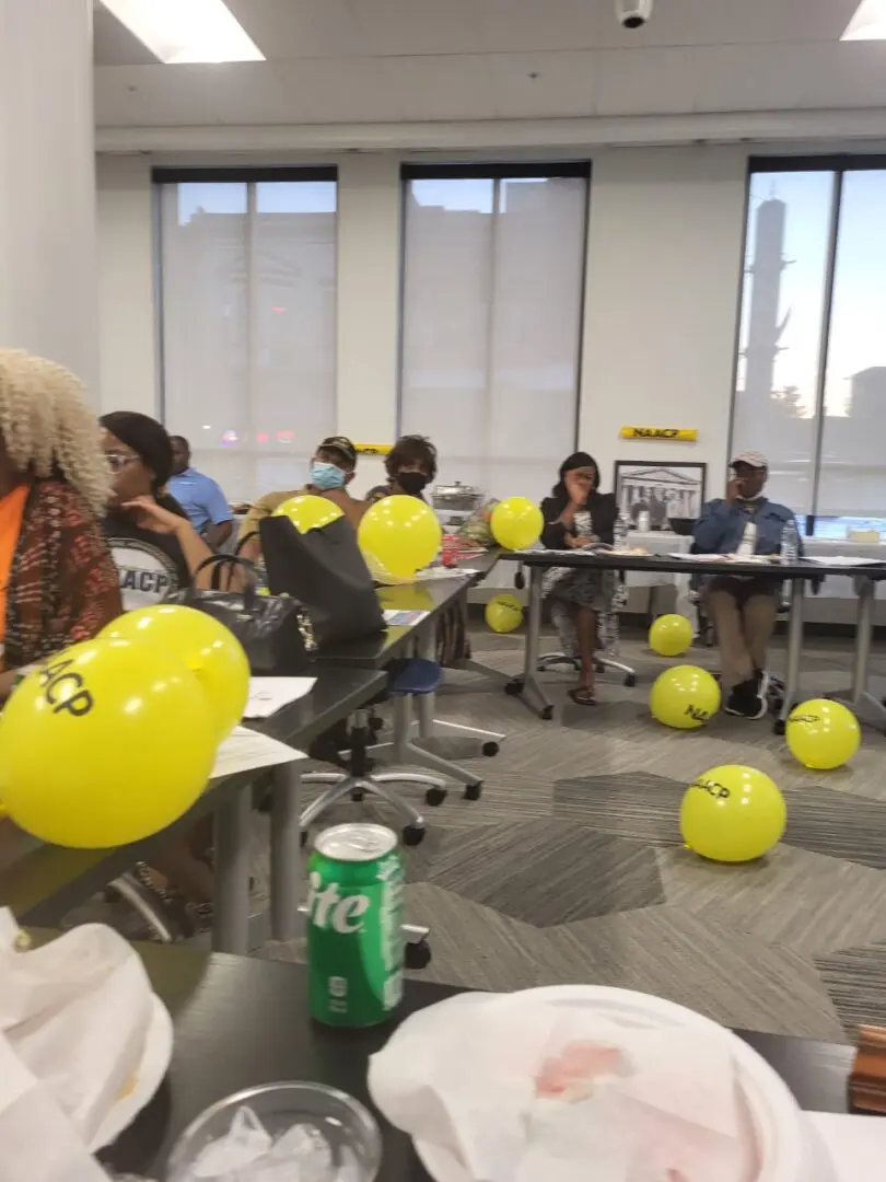 A group of people sitting around tables with yellow balloons.