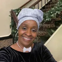 A woman with a head wrap on sitting in front of stairs.